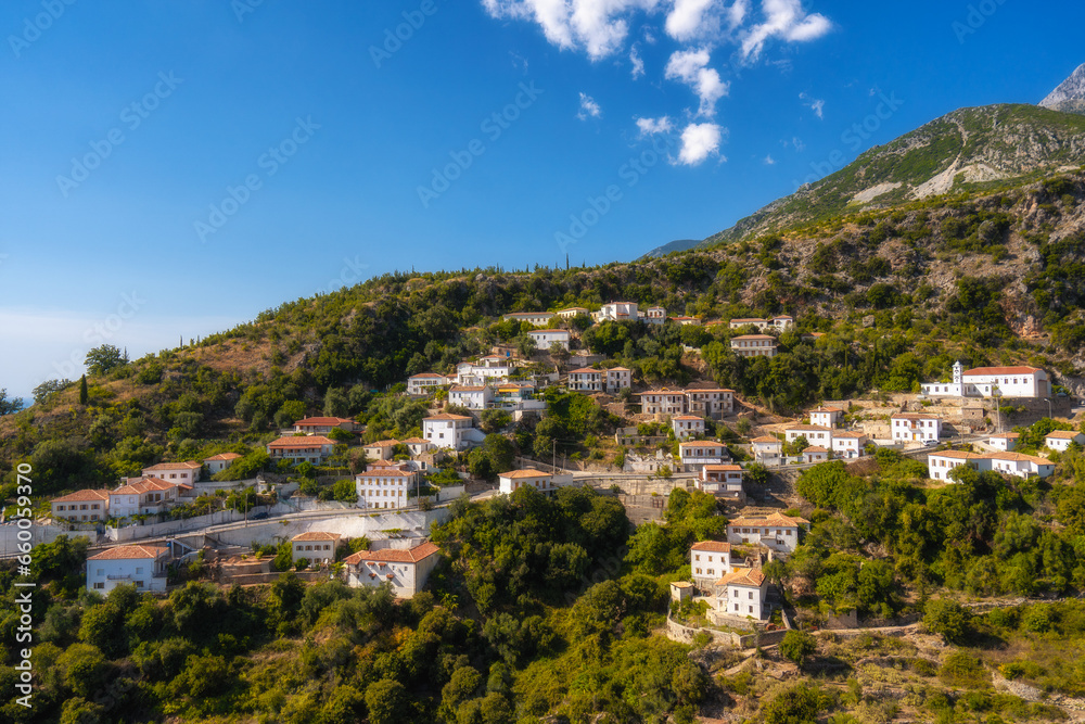 View of white houses with yellow shutters, moutains and sea. Vuno, Albania.