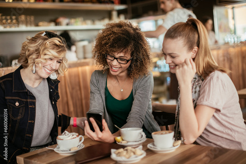 Diverse trio of female friends using the smartphone together in a cafe or bar