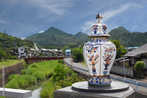 A porcelain vase in the traditional Japanese Imari style - red, blue and gold colours, picturesque landscape of the town of Arita in the background. 
