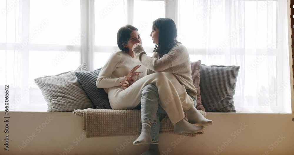 Couple, lgbt and lesbian women at home. Portrait of lesbian couple enjoying. Young lesbian couple smiling and touching hands gently while sitting on sofa against window in light living room at home. Couple, lgbt and lesbian women at home. Portrait of lesbian couple enjoying. Young lesbian couple smiling and touching hands gently while sitting on sofa against window in light living room at home.