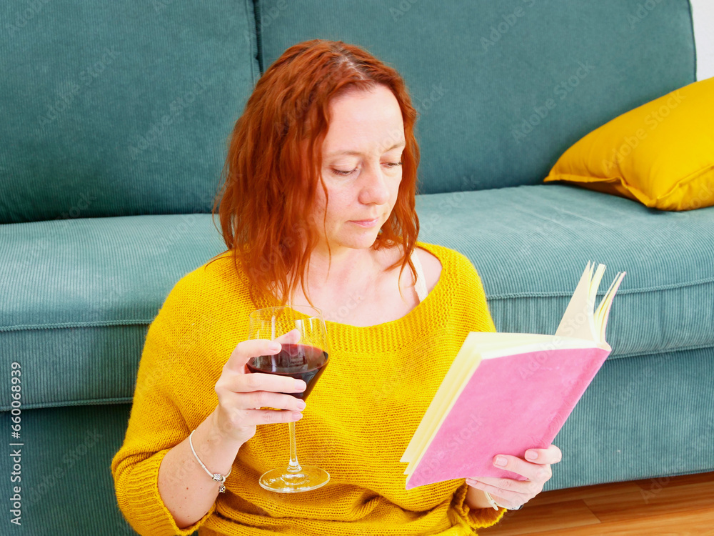Woman relaxing at home, reading diary or book with the glass of wine