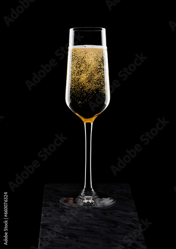 Elegant glass of yellow champagne with bubbles on black marble board on black background.