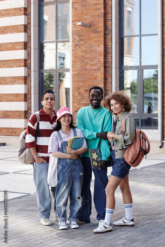 Vertical full length portrait of multiethnic group of students smiling at camera standing outdoors on college campus