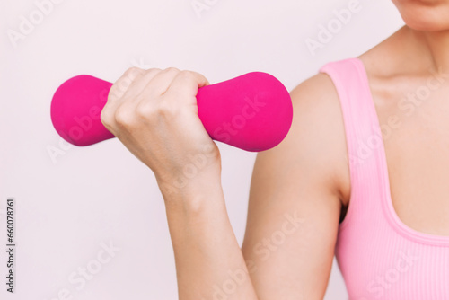 Bright pink dumbbell in the hand of young athlete woman demonstrating her strength and power doing biceps exercises. Fitness, workout, sports. Sporty girl on a white background