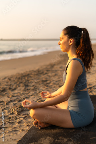 vertical photo of a lady sitting in zen pose in front of the beach