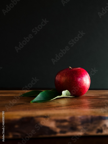 Single apple with leaf on dark background wooden table moody feeling