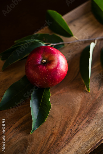 Single red apple on wooden cutting board with branch and leaves moody organic autumn feeling