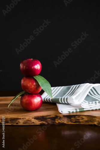 Three stacked bright red apples with white striped kitchen towel on wooden cutting board dark moody rustic background fall feeling