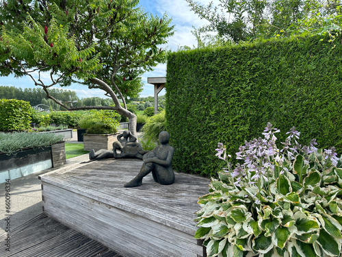 Appeltern, Netherlands, July 11, 2023: Beautiful roof garden. Wooden decking.  Garden sculptures, Thuja plicata and blooming Agapanthus praecox on the foreground photo