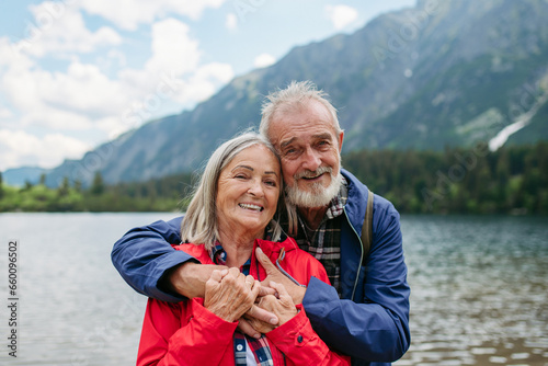Active elderly couple hiking together in autumn mountains. Senior spouses on the vacation in the mountains celebrating anniversary. Senior tourists embrancing each other in front of lake. © Halfpoint