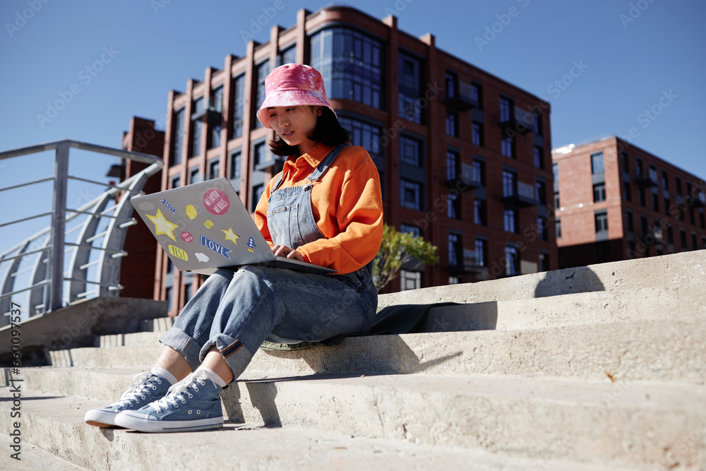 Colorful portrait of two Asian young woman using computer outdoors sitting on concrete stairs in sunlight, copy space