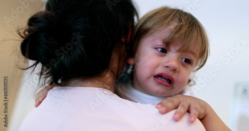 Tearful baby boy. Mother wearing surgical mask holding upset crying infant