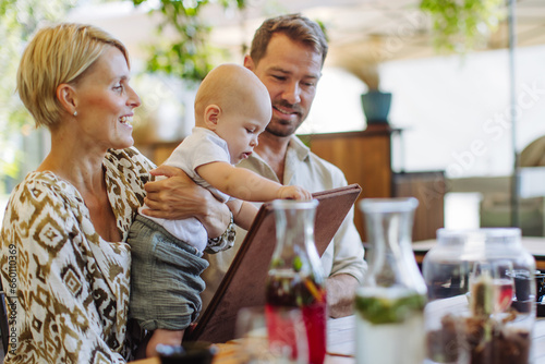 Family with little baby in a restaurant, choosing food and drinks.