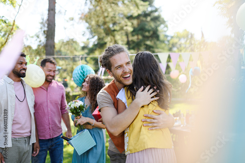 Friends reunite after a long time apart. Men and women embracing, happy to meet at garden party.