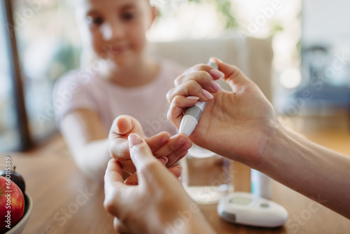 Close up of mother checking girl's blood glucose level using fingerstick glucose meter. Endocrinologist waiting for results from blood test. photo