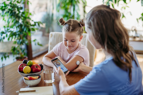 Girl with diabetes checking blood glucose level at home using continuous glucose monitor. Mother connects CGM to a smartphone to monitor her blood sugar levels in real time. photo