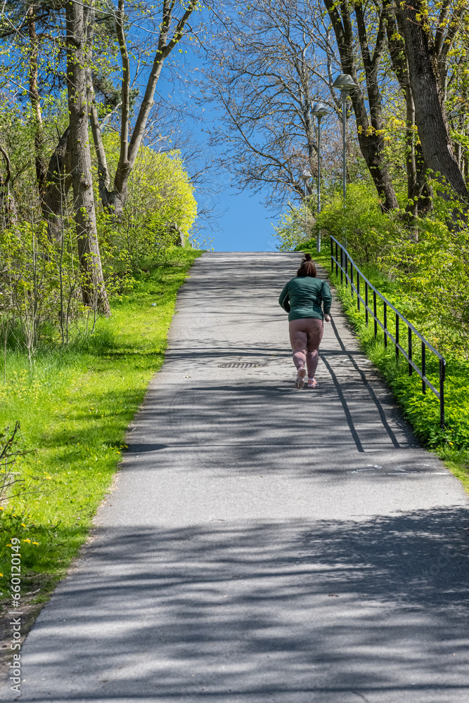 Fototapeta premium Woman jogging up a steep hill in spring.