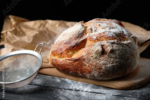 fresh loaf of bread sprinkled with flour on a wooden background