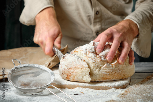 man slices fresh bread on a wooden table