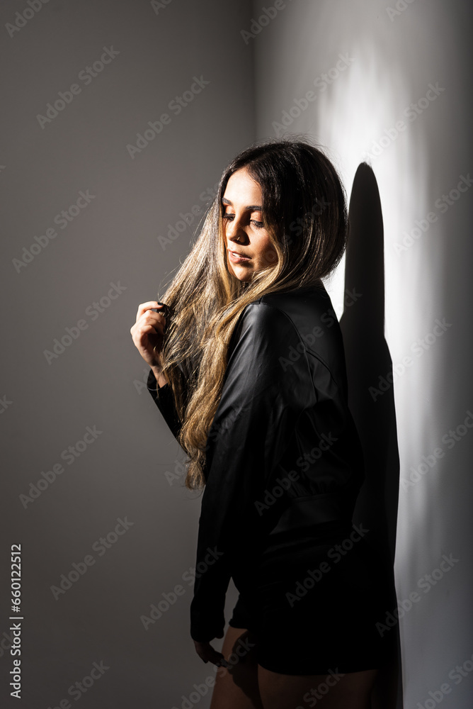 Portrait of beautiful young woman wearing black clothes leaning against a white wall.