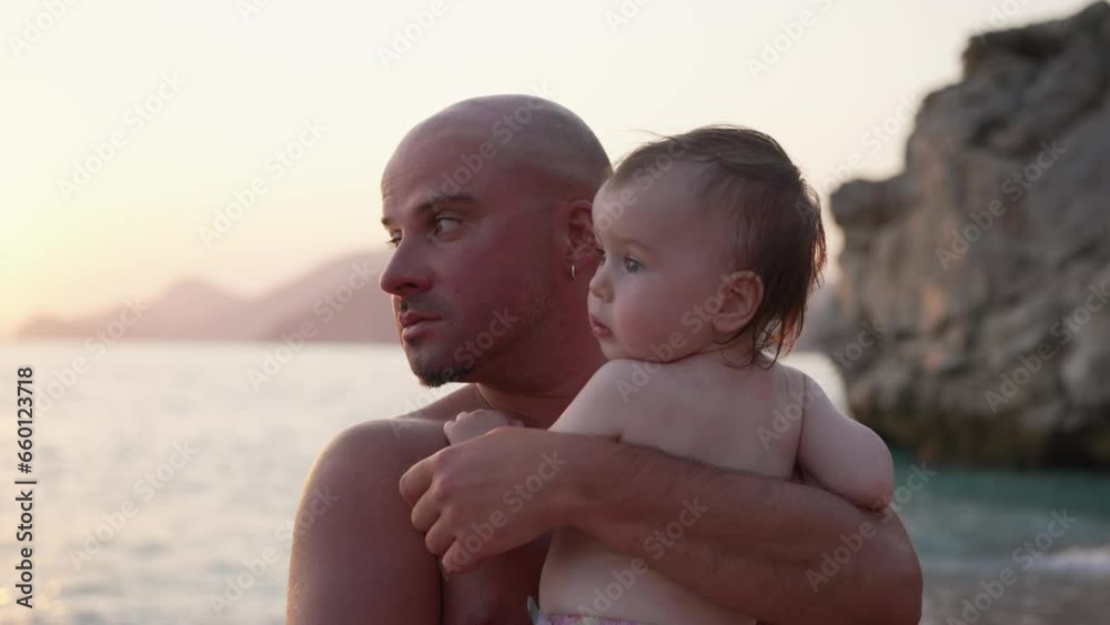 Young Happy Sporty Father Hugging his Newborn Baby on Sea Beach at Sunset Young Happy Sporty Father Hugging his Newborn Baby on Sea Beach at Sunset
