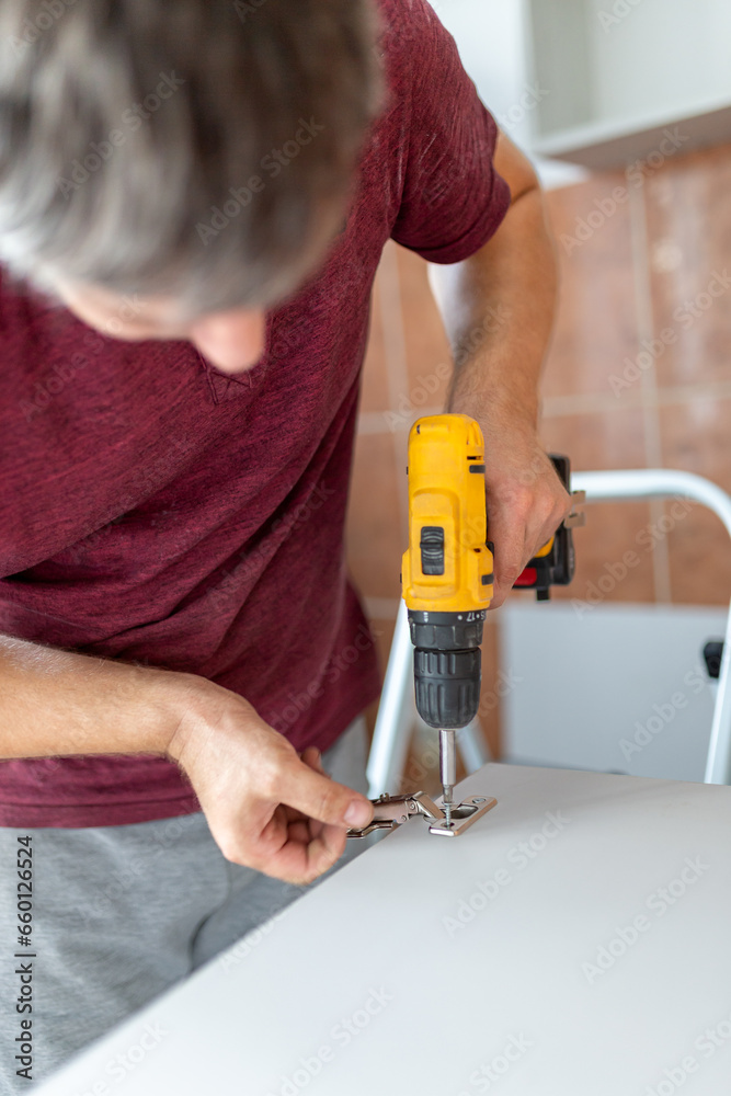 Man holding cordless screwdriver machine and screws lie for screwing a screw assembling furniture at home
