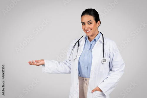Happy latin doctor presenting invisible item on her palm over grey studio background
