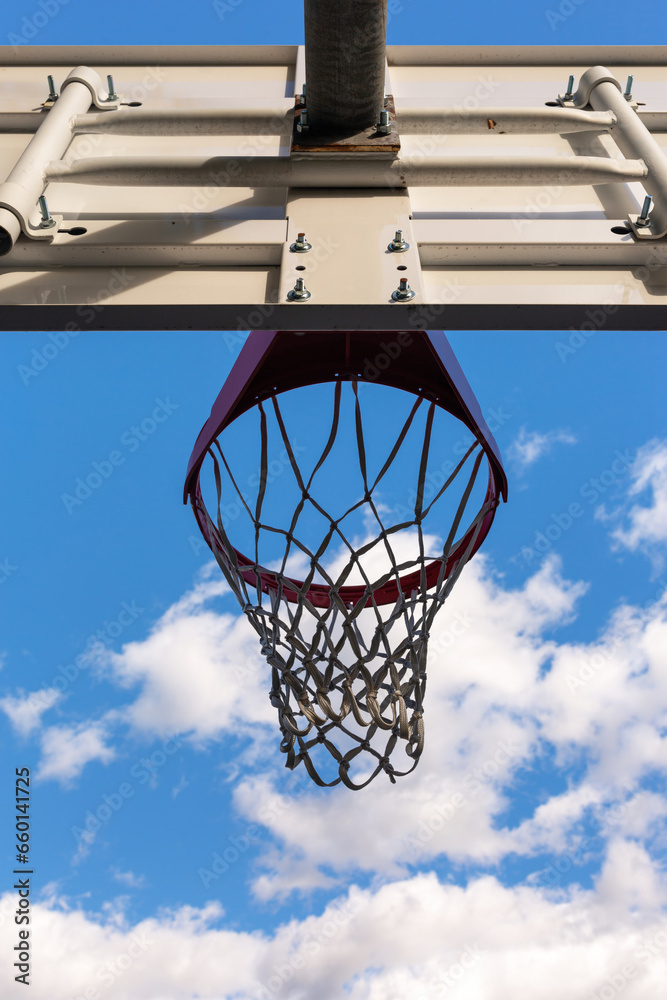 ?A basketball hoop with a net on a court against a backdrop of blue skies and fluffy white clouds, offering the perfect setting for outdoor sports and recreation.