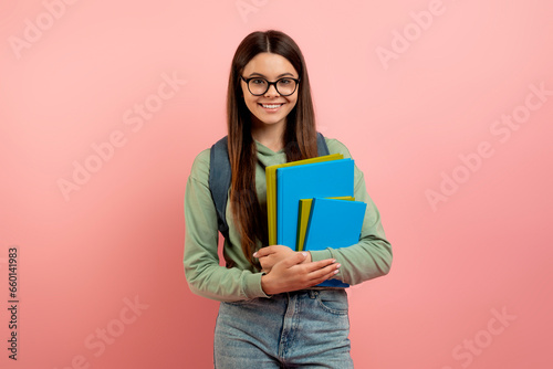 Portrait of smiling teenage girl student with backpack, workbooks, and eyeglasses