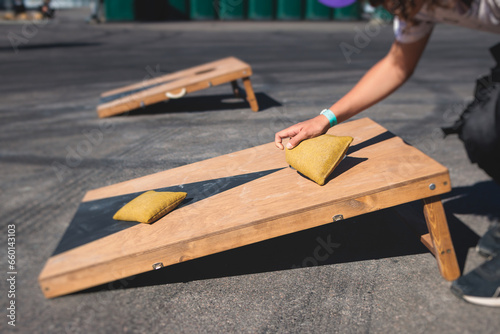 Cornhole game set, process of throwing bean bags, kids children tossing bean sacks, corn hole  in the backyard, wooden boards for corn-hole tournament in the summer sunny day photo