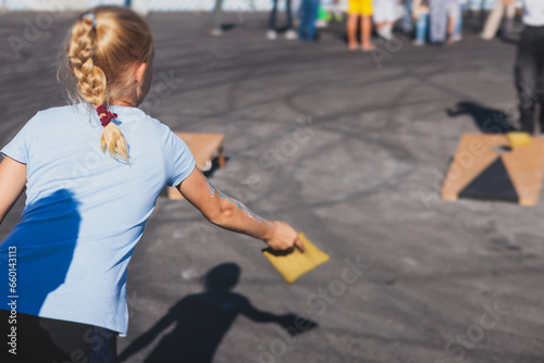 Cornhole game set, process of throwing bean bags, kids children tossing bean sacks, corn hole  in the backyard, wooden boards for corn-hole tournament in the summer sunny day