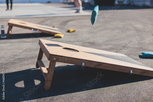 Cornhole game set, process of throwing bean bags, kids children tossing bean sacks, corn hole  in the backyard, wooden boards for corn-hole tournament in the summer sunny day photo