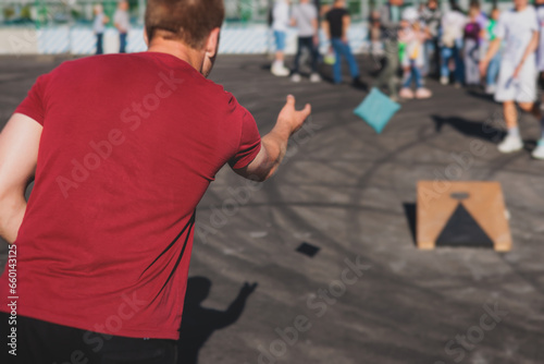 Cornhole game set, process of throwing bean bags, kids children tossing bean sacks, corn hole  in the backyard, wooden boards for corn-hole tournament in the summer sunny day
