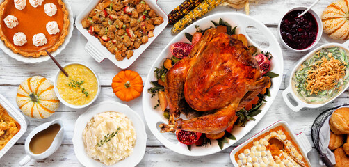 Delicious Thanksgiving turkey dinner. Overhead view table scene on a rustic white wood banner background. Turkey, mashed potatoes, stuffing, pumpkin pie and sides.