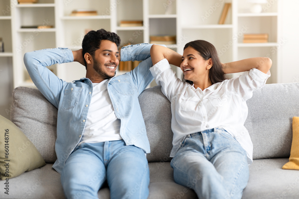 Happy indian couple on sofa, hands behind head, smiling at each other Happy indian couple on sofa, hands behind head, smiling at each other