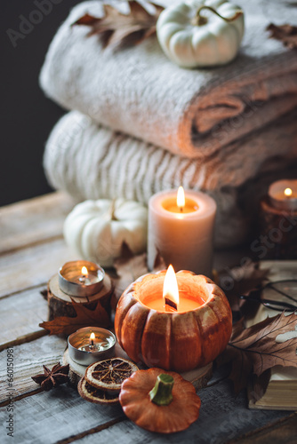 Atmospheric candle - shape of pumpkins, autumn decor, book on grey fall rainy day. Autumn cozy home atmosphere, inspiration, hygge concept. Aromatherapy, warming, relaxation. Wooden background