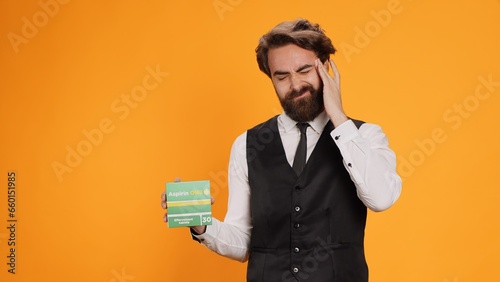 Obraz na plátne Classy waiter with headache recommends pills on camera, showcasing pack of painkillers to ease pain