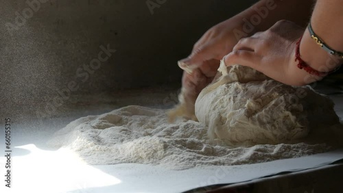 Female hands knead the dough on a black background in a rustic style. Flour flies in the air