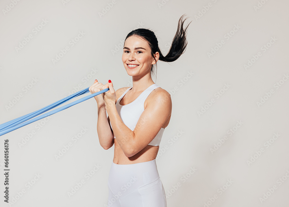 Smiling woman doing biceps curl with resistance band at white wall Smiling woman doing biceps curl with resistance band at white wall