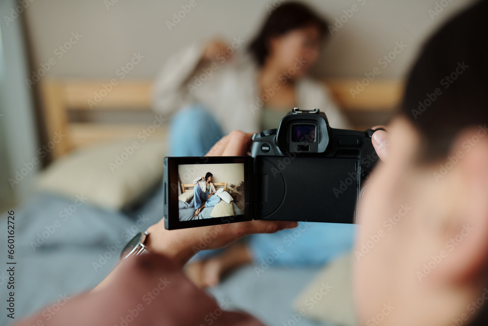 Focus on screen of photocamera held by photographer taking pictures of female fashion model relaxing on double bed during photo shooting