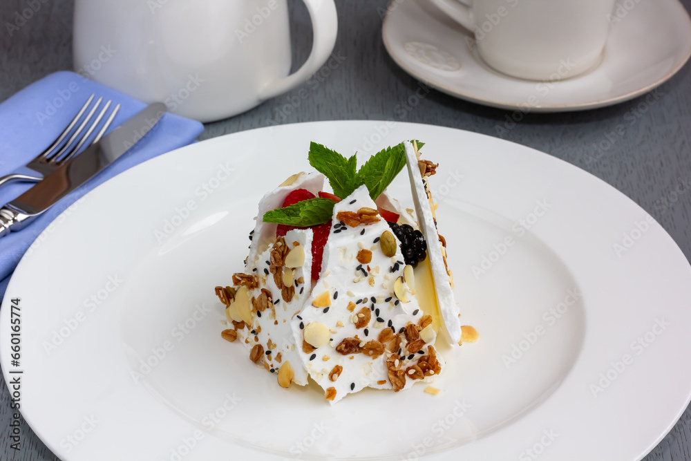 An airy meringue cake with whipped cream is decorated with blueberries, strawberries and mint leaves. Pavlov's dessert. Vertical. Dessert. An airy meringue cake with whipped cream is decorated with blueberries, strawberries and mint leaves. Pavlov's dessert. Vertical. Dessert.
