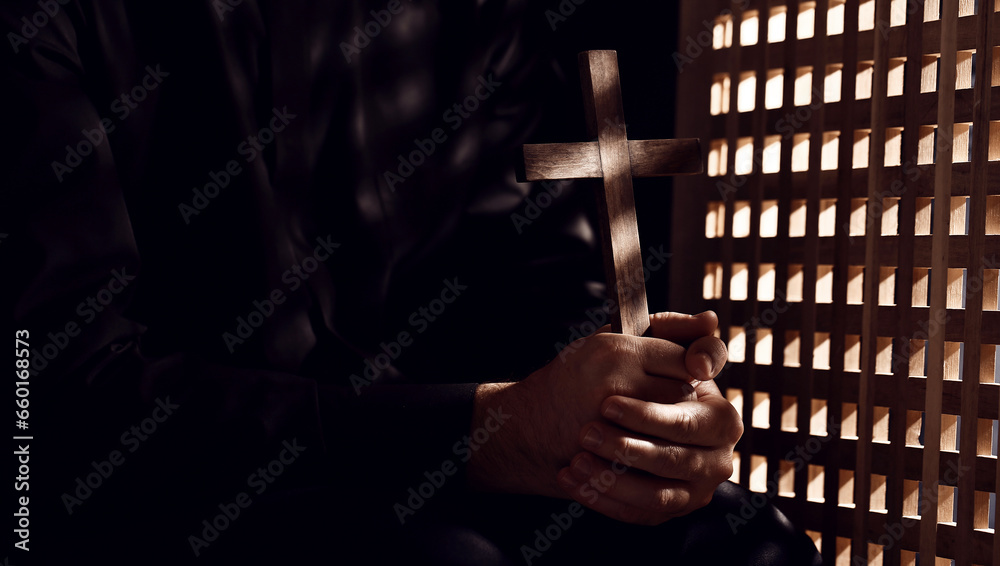 Young priest with cross in confession booth - obrazy, fototapety, plakaty 
