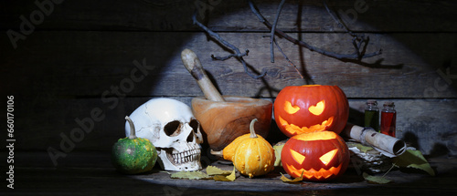 Halloween pumpkins, skull, mortar with pestle and autumn leaves on table against wooden background