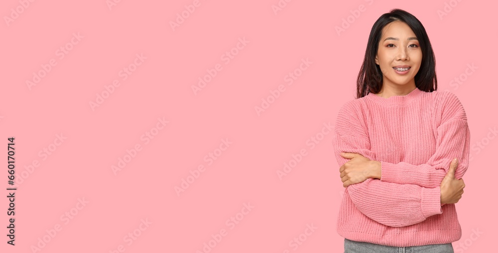 Fototapeta premium Young Asian woman hugging herself on pink background with space for text