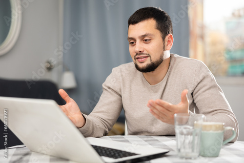 Smiling man chatting online using laptop at home