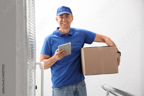 Mature courier with tablet computer and parcel in stairway © Pixel-Shot