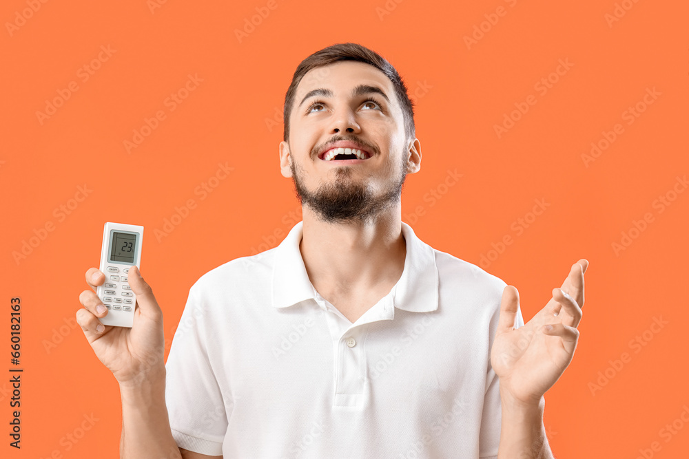 Young man with air conditioner remote control on red background