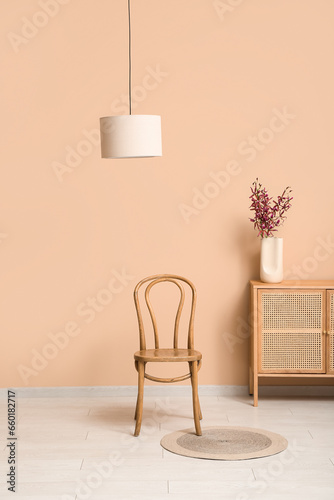 Wooden chair  chest of drawers and vase with flowers near color wall in room