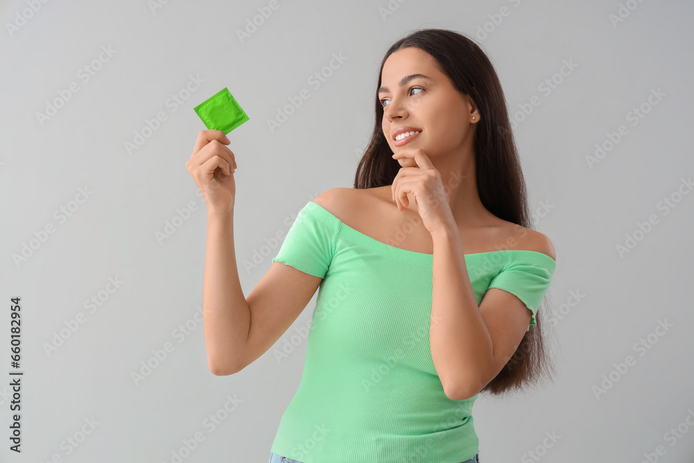 Thoughtful young woman with condom on light background Thoughtful young woman with condom on light background