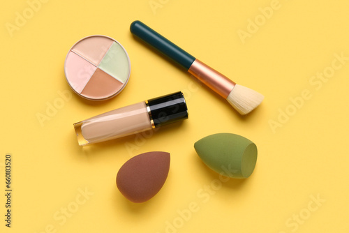 Makeup sponges and decorative cosmetics on yellow background